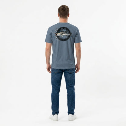 A man viewed from behind wearing a slate blue t-shirt with a striped bass fish graphic on the back, paired with blue jeans and white sneakers, against a plain white studio background.
