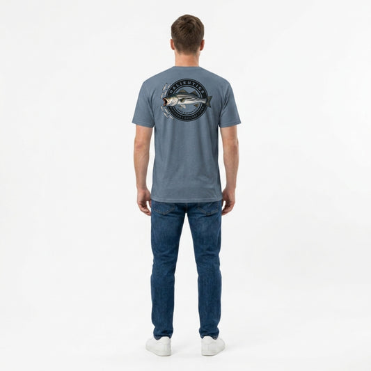 A man viewed from behind wearing a slate blue t-shirt with a striped bass fish graphic on the back, paired with blue jeans and white sneakers, against a plain white studio background.